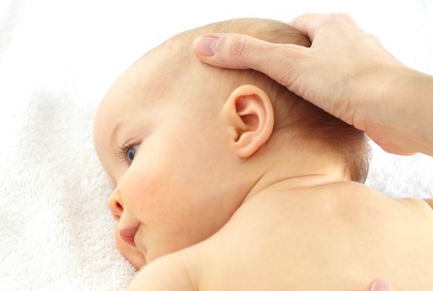 Button-Kinderosteopathie2 Baby liegt auf einem Handtuch und wird am Kopf massiert
